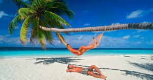 Couple chilling out with hammock under palm trees and sunny skies on white sandy beach in Maldives